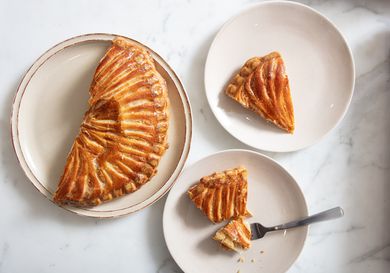 2 plates of Galette des Roi, one with a fork full of cake. A third plate with the remaining galette on it 