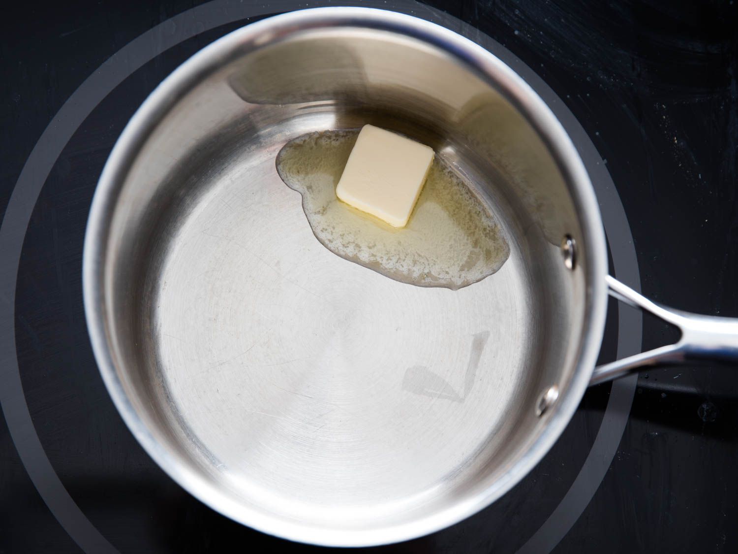 Overhead shot of a pat of butter being melted in a saucepan.