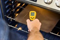A person using an infrared thermometer to take the temperature of a baking steel.