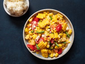 Overhead of a serving plate of corn salad with a bowl of sticky rice on the side.