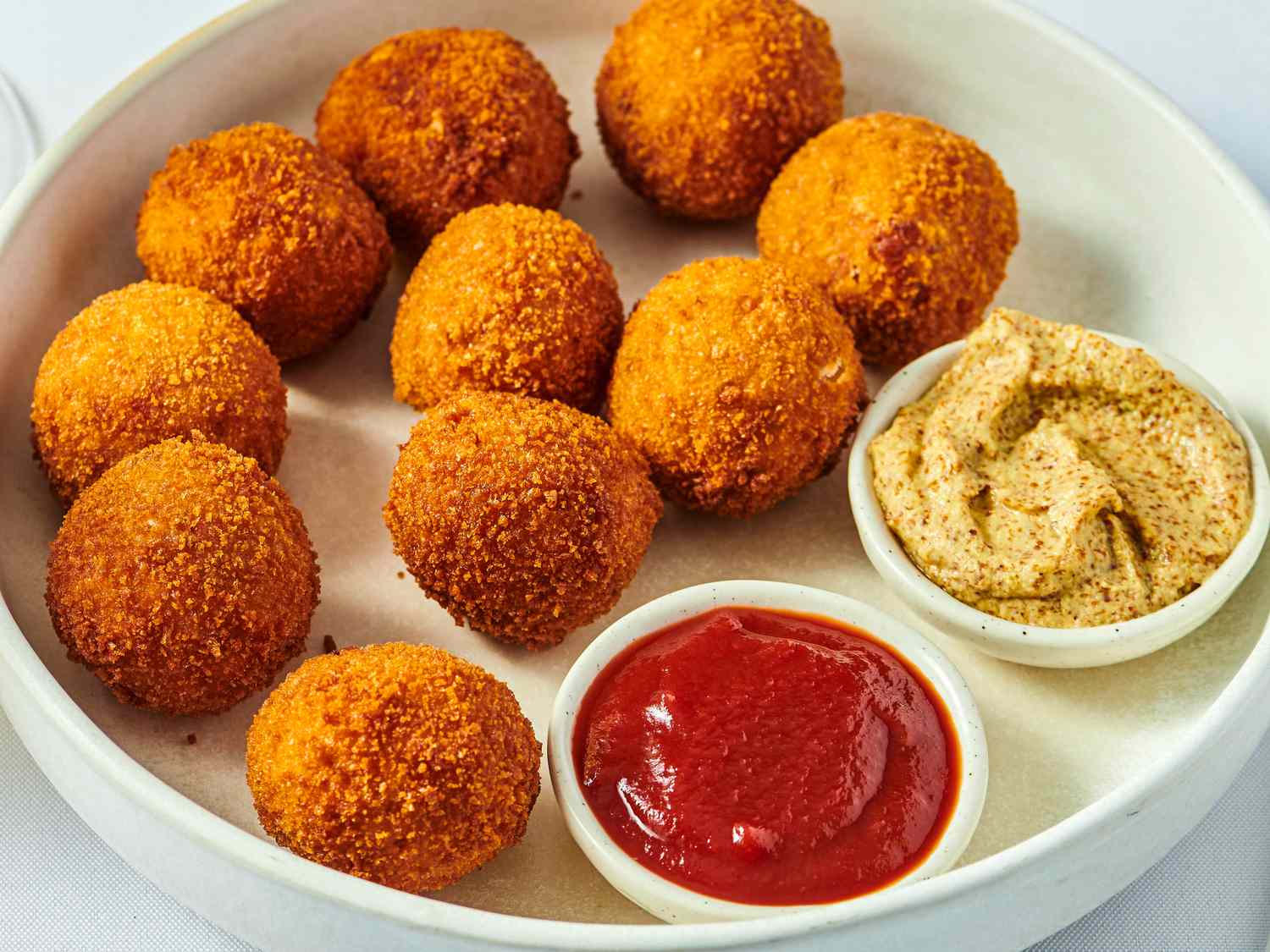 Plate of Ohio sauerkraut balls with one ball open, small bowls of ketchup and mustard.