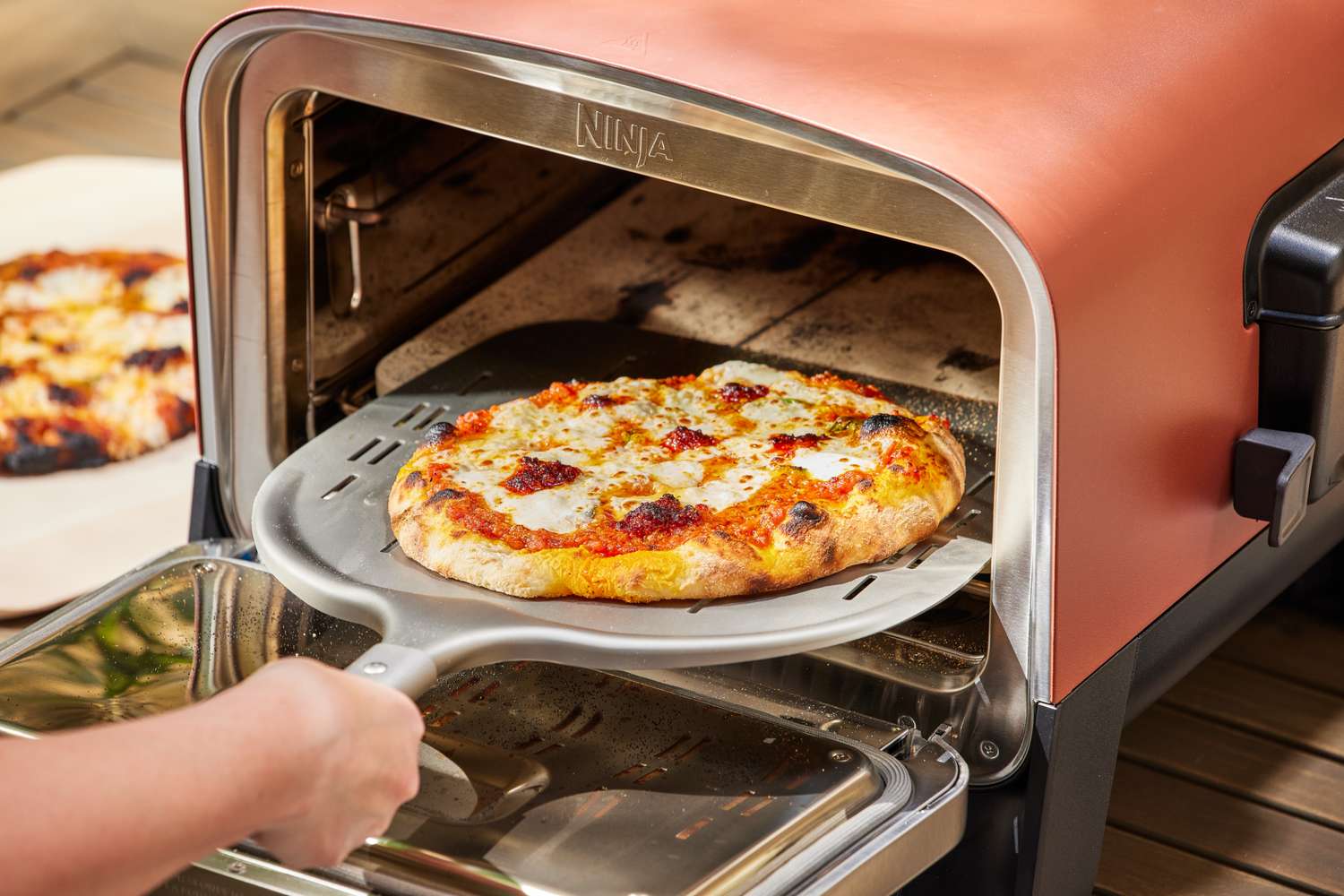 A close-up of a hand removing a pizza from the Ninja Woodfire 8-in-1 Outdoor Oven
