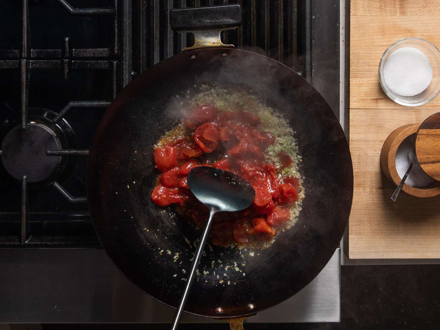 Tomatoes added to garlic and scallions in a wok.