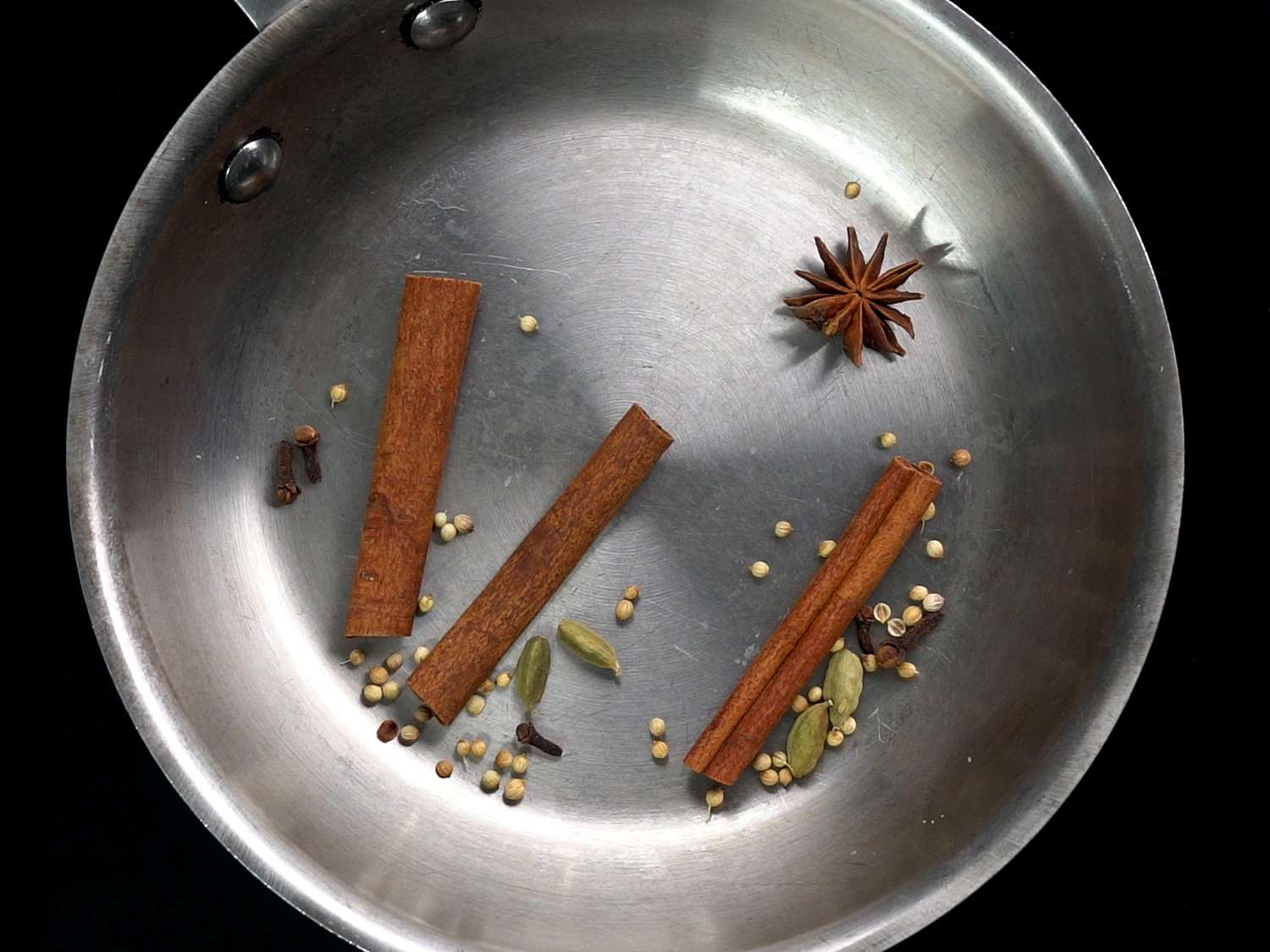 Overhead shot of mulling spices (cinnamon stick, star anise, cardamom, coriander, and cloves) for cider in a large pot