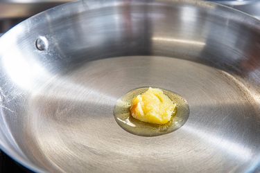 A piece of ghee melting in a stainless steel frying pan on a stove