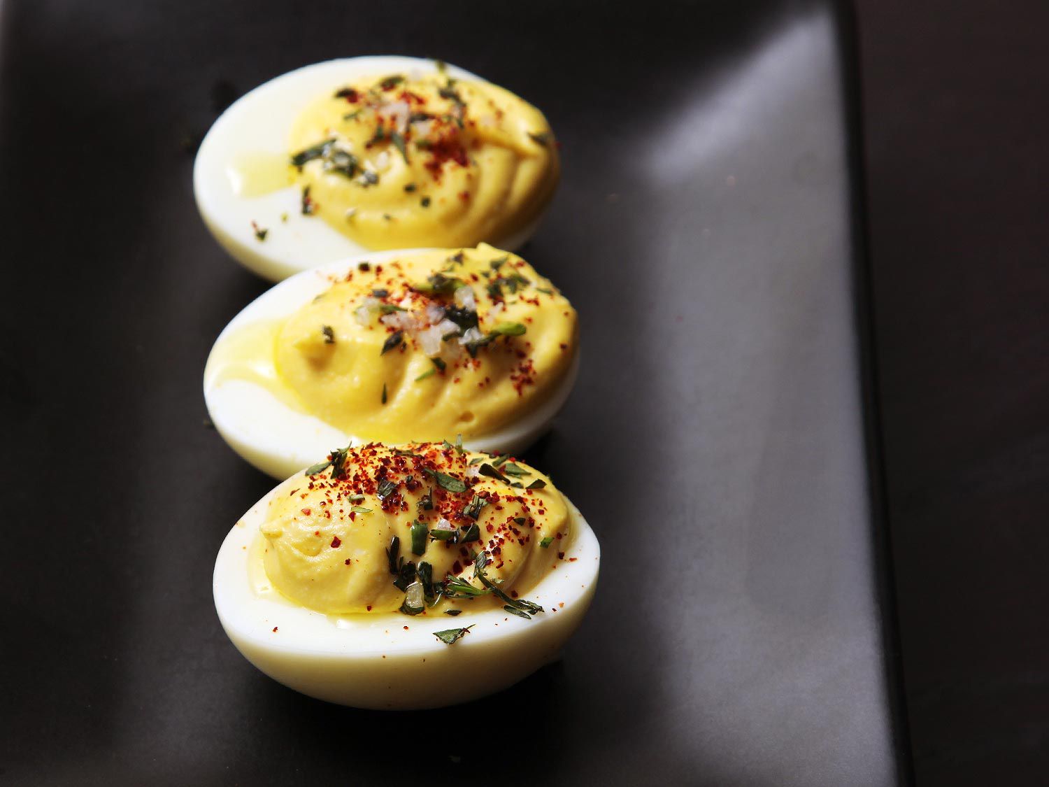A row of three deviled eggs on a black plate