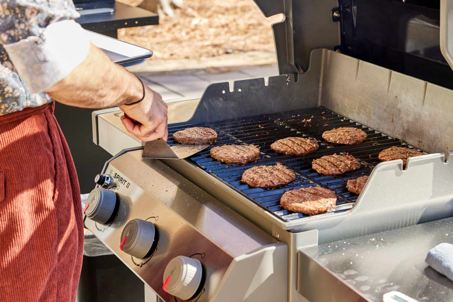 a person flipping burgers on a gas grill