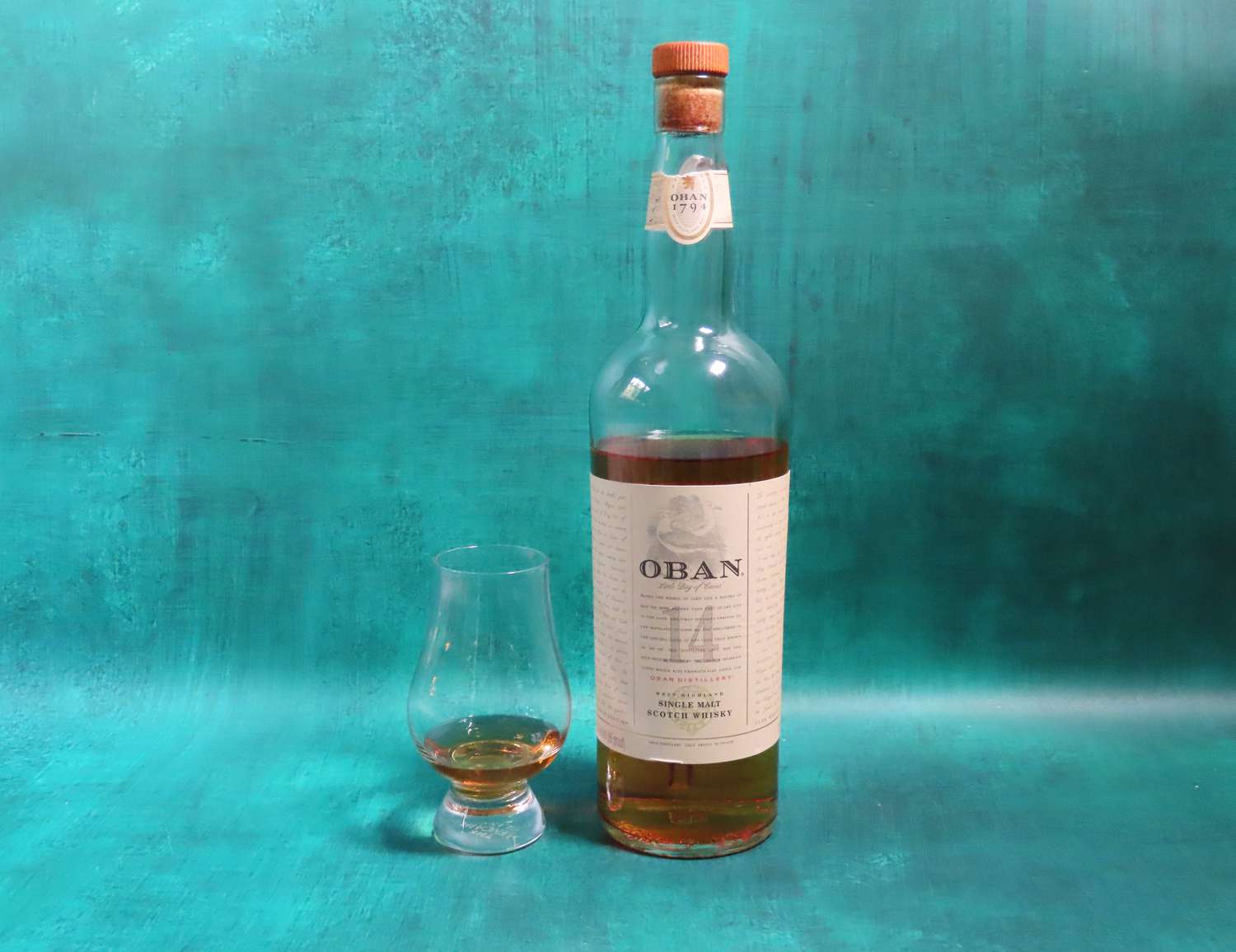 a bottle of Oban whisky on a blue surface with a whisky glass beside it