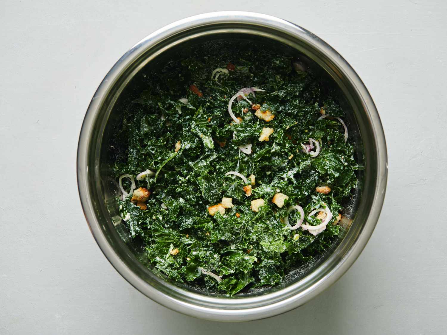  Onions, dressing, half of croutons, and wilted kale tossed until thoroughly coated inside a large bowl.