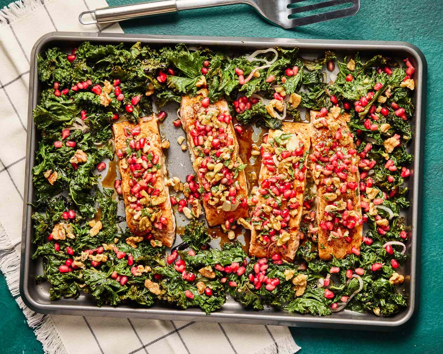 Salmon fillets topped with pomegranate seeds and greens on a baking sheet