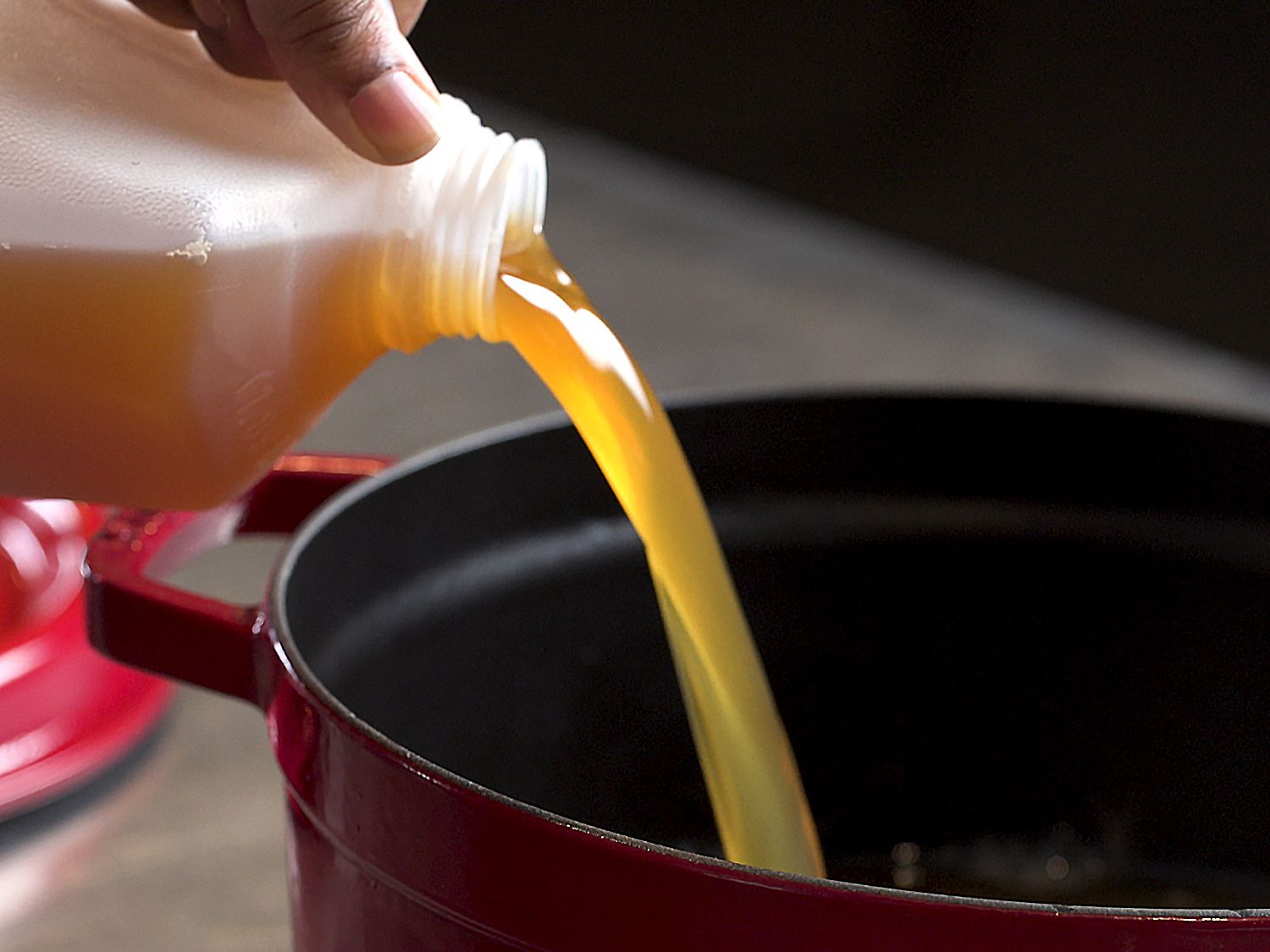 Apple cider pouring from a jug into a large red pot
