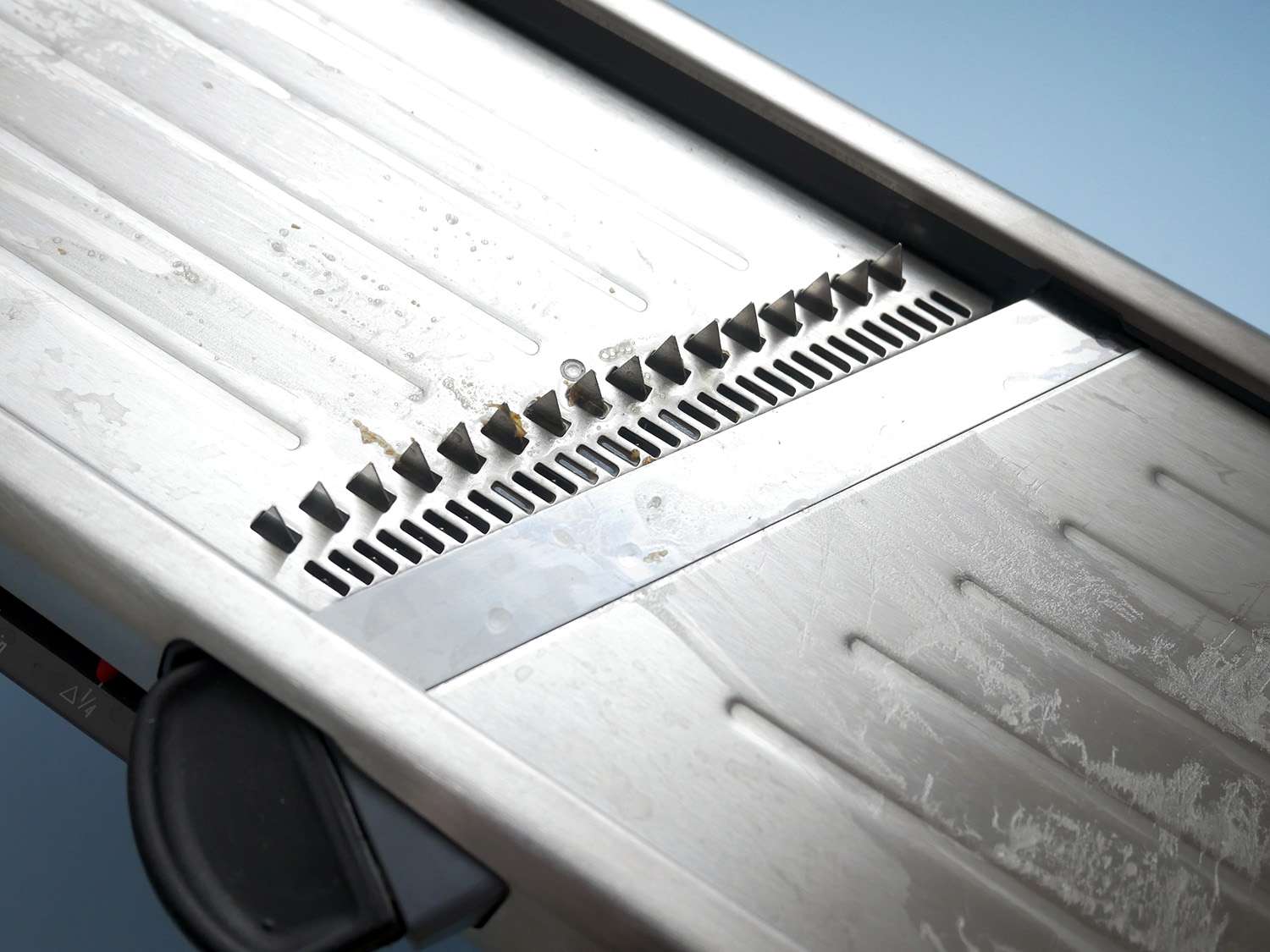 closeup of julienne and slicer blade on oxo steel mandoline. bits of potato are stuck on the julienne blades. 