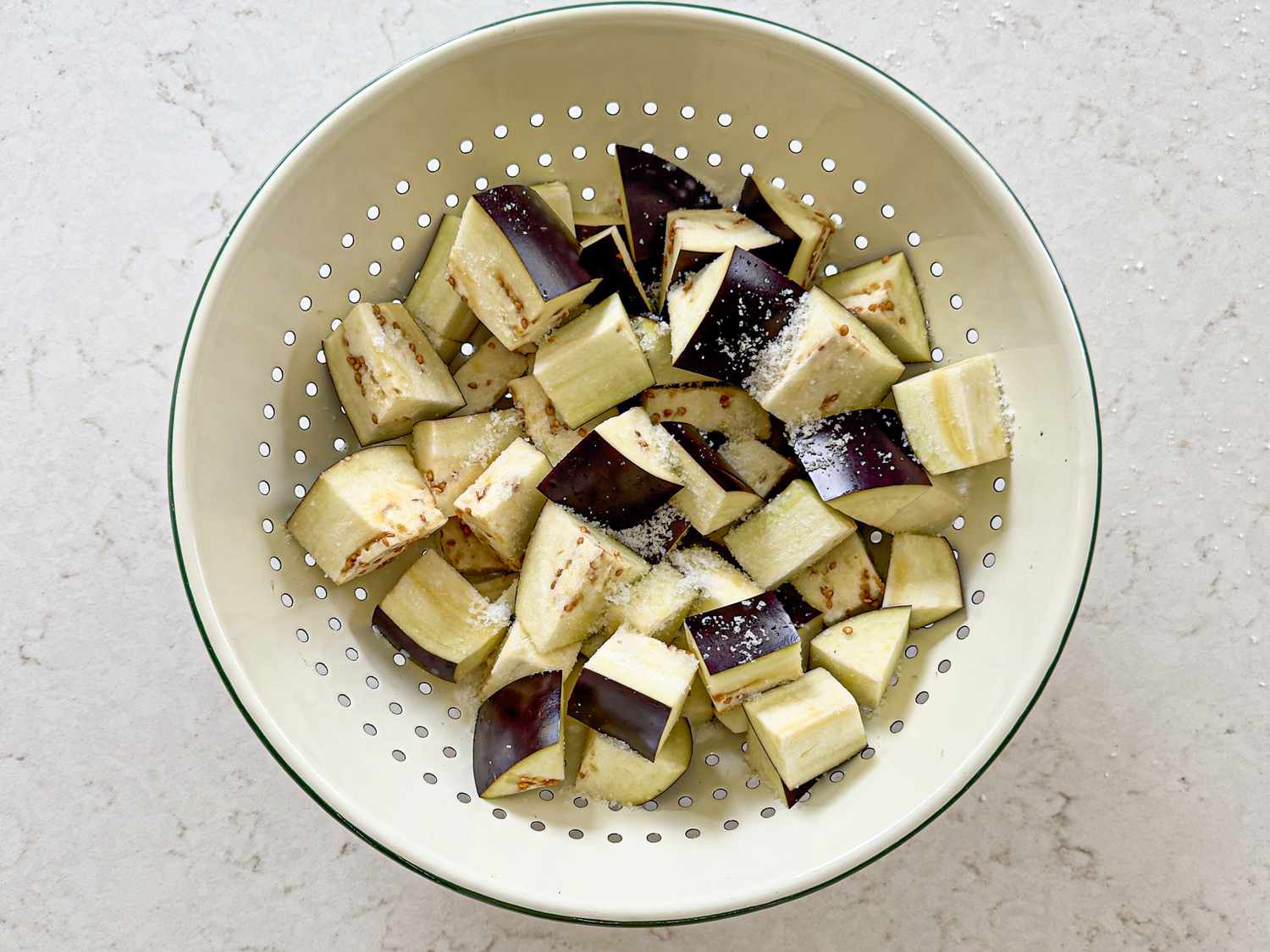 Chopped eggplants in a colander being salted for preparation