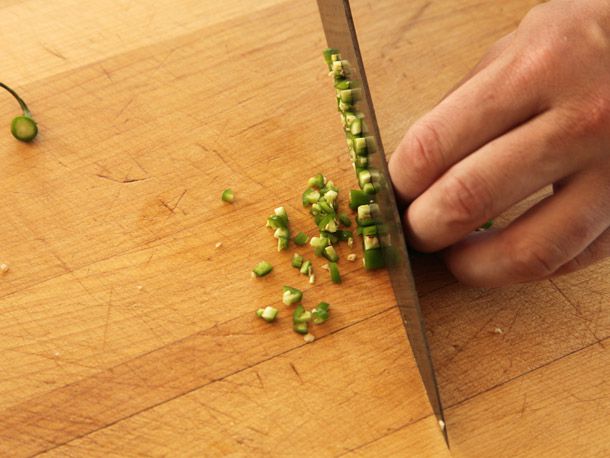 Tucked fingers against chef's knife cutting green pepper into fine dice on wooden cutting board