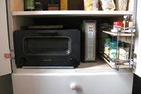 Kitchen cabinet with a Balmuda toaster oven olive oil and various spice containers on shelves