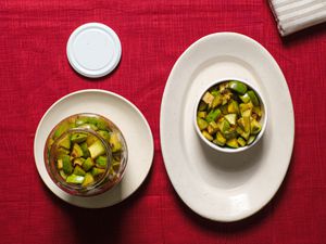 Mango pickle in a glass jar, and in a ramekin on a plate, on top of a red tablecloth