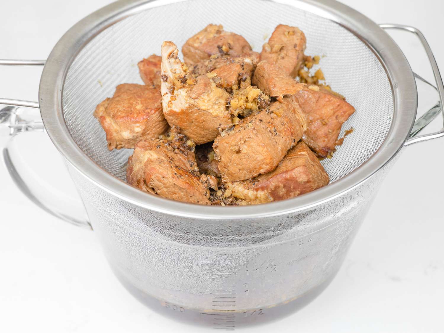 Cooked pork pieces in a strainer set in a large measuring cup