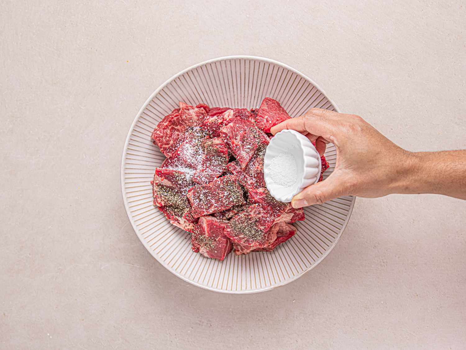 Raw beef in a bowl being sprinkled with salt 