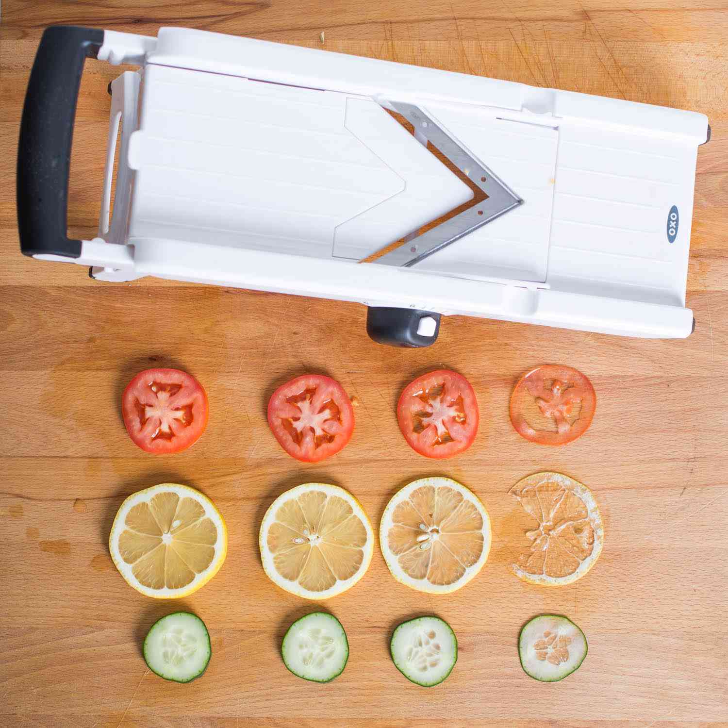 Thin slices of tomatoes, lemon, and cucumber next to the OXO Mandoline