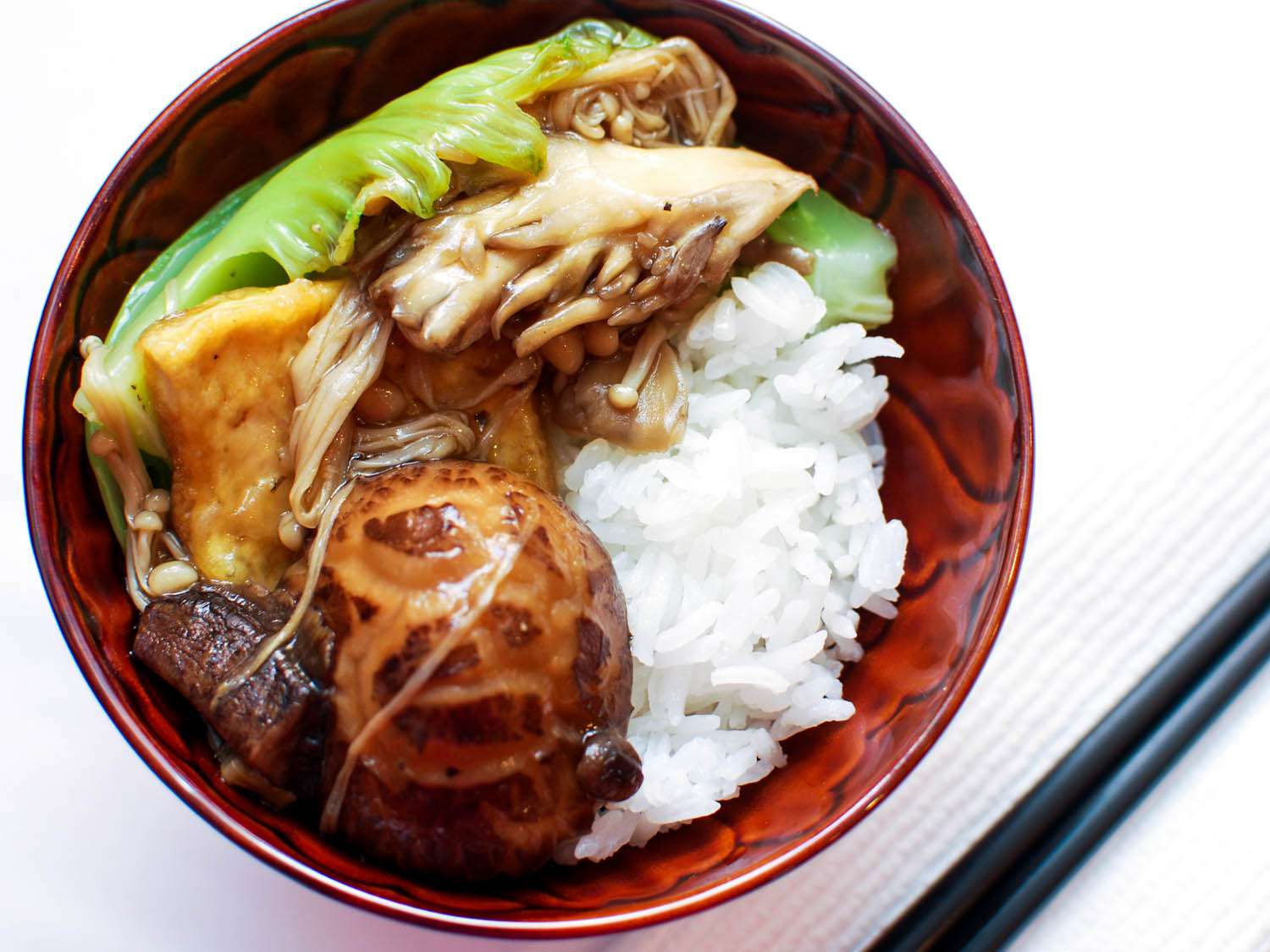 Overhead view of rice bowl topped with braised assorted mushrooms, tofu, and Chinese mustard greens