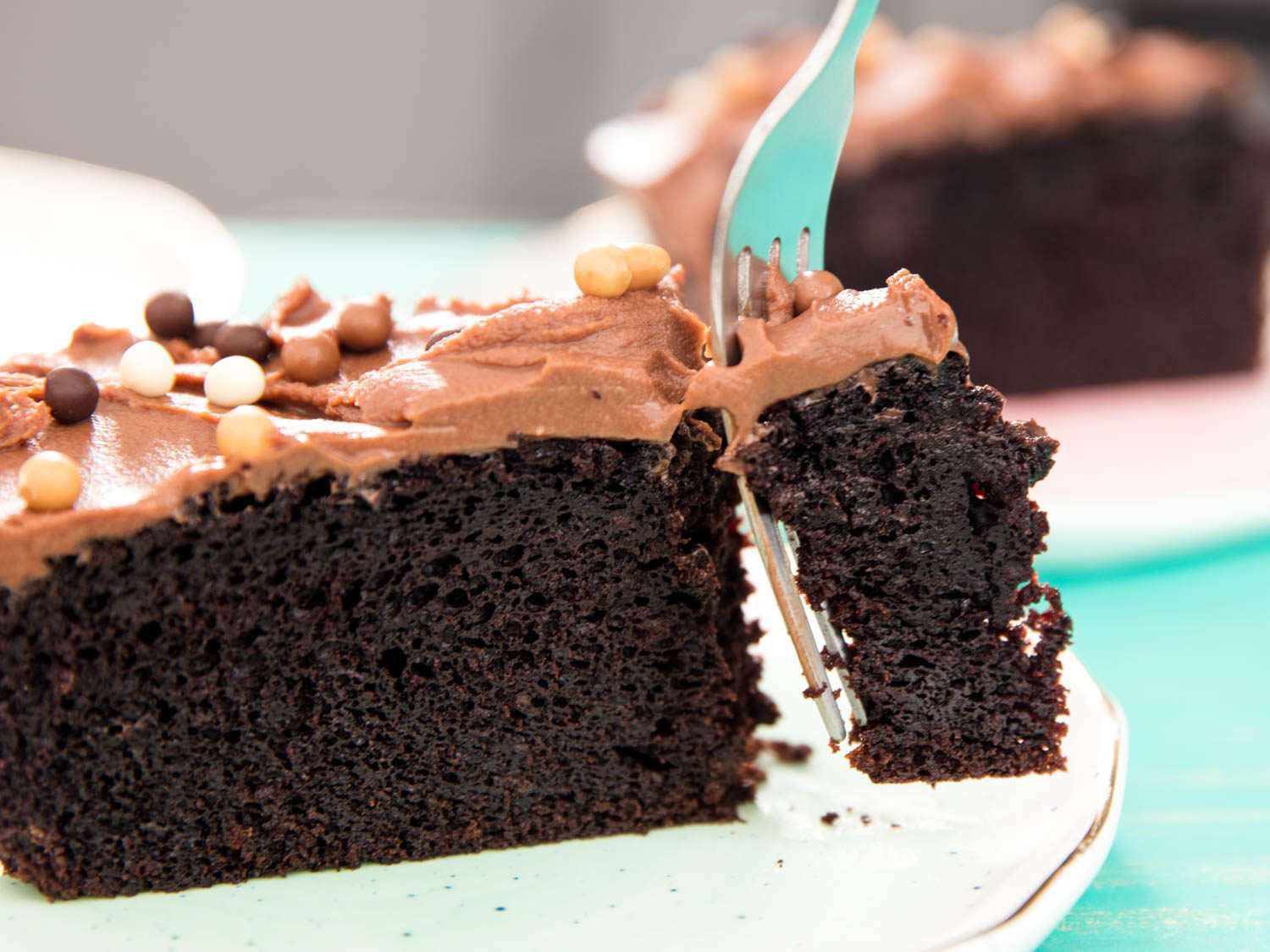 Close-up of a fork spearing a bite of chocolate skillet cake topped with milk-chocolate frosting and crunchy pearls.