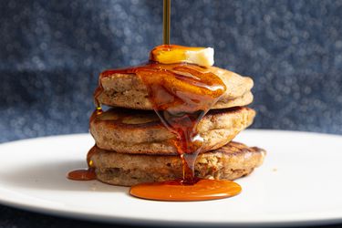 stack of banana bread pancakes with butter on top and syrup pouring over them on a white plate
