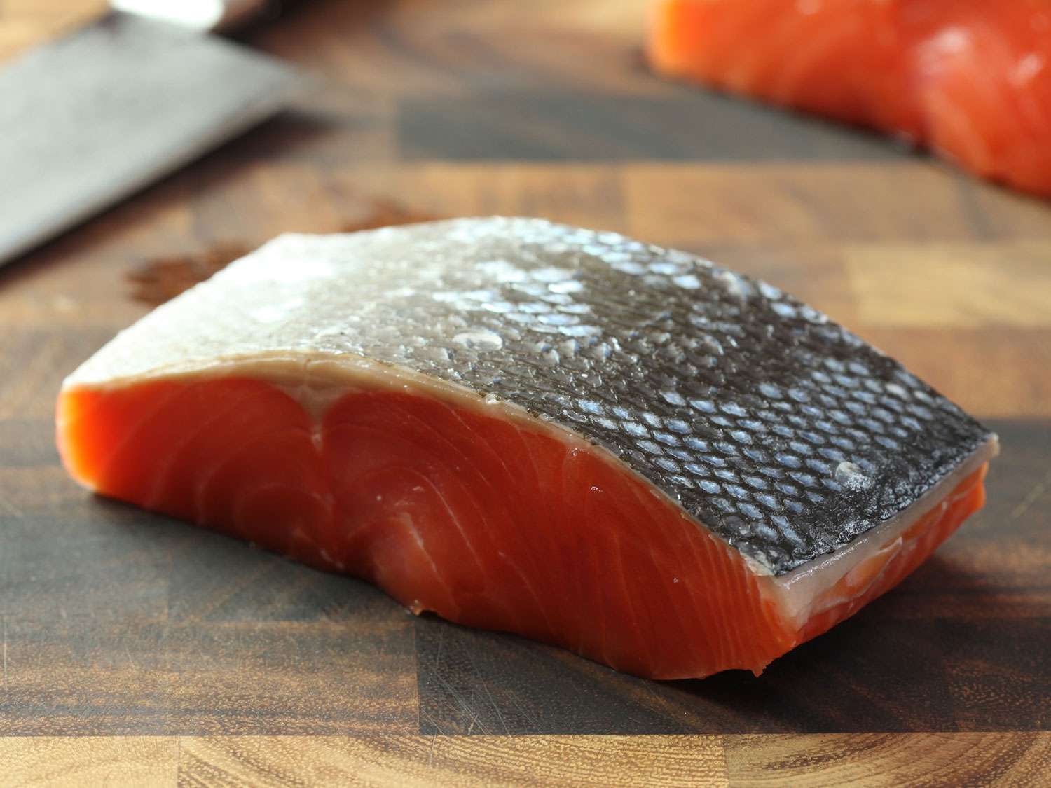 Raw, skin-on salmon fillet sitting skin-side up on a wooden cutting board.