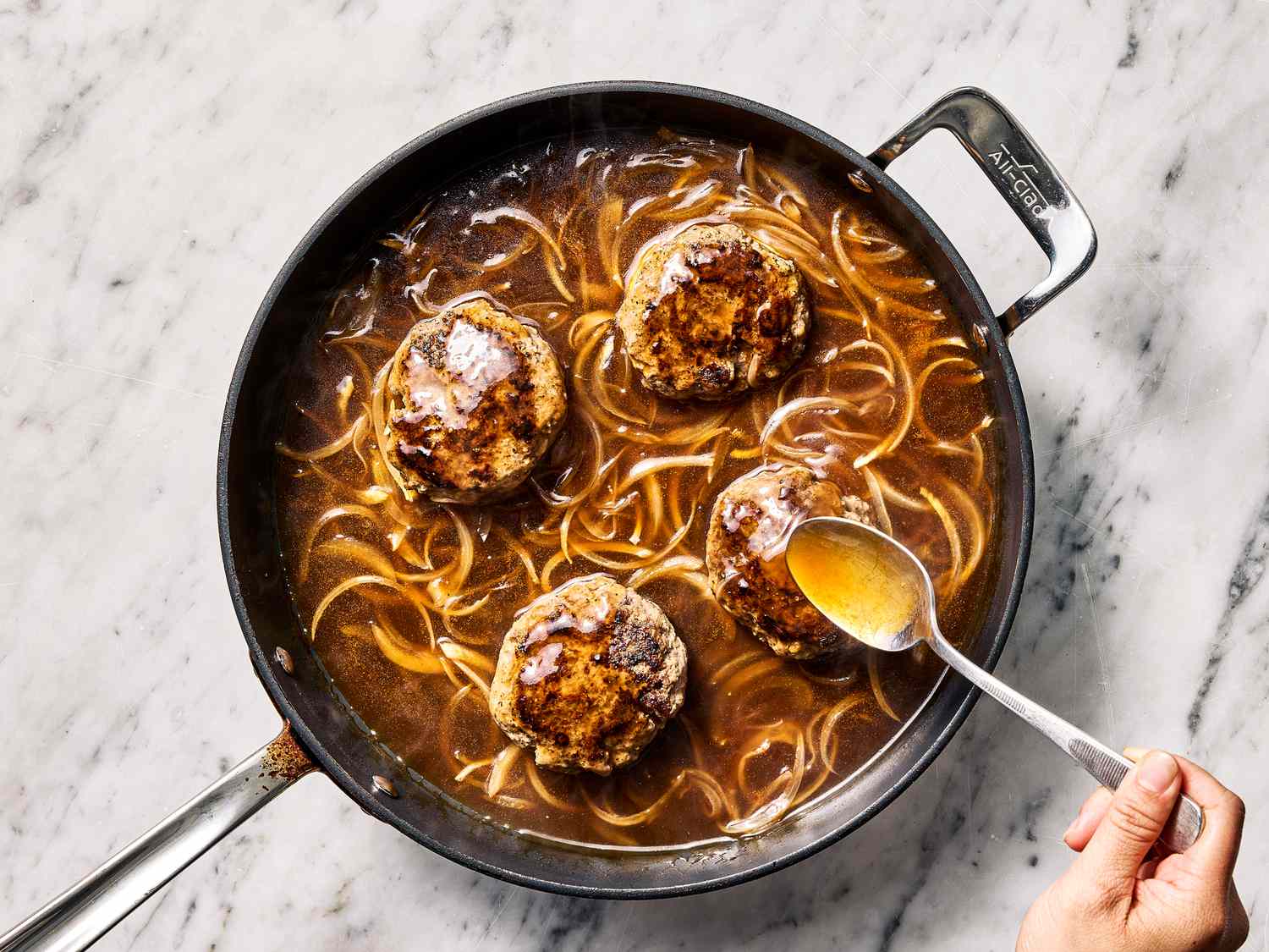 Pan with meat patties and gravy, spoon stirring liquid