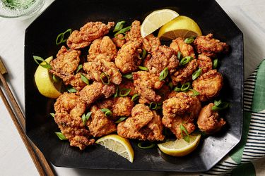 Fried Japanese chicken on a black plate with chopsticks, lemon, and a stylish napkin