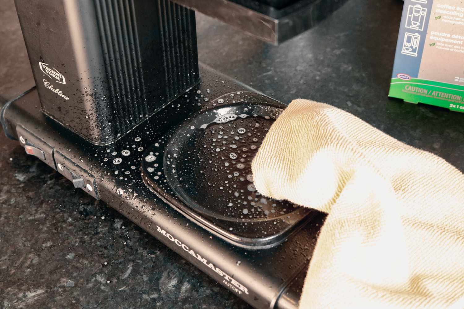 Using a yellow microfiber cloth to wipe down the exterior of a coffee maker