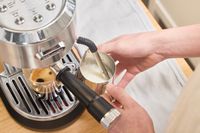 A person froths milk using the De'Longhi EC900M Dedica Maestro Espresso Machine