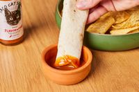 Person dipping tortilla into Flavor and Fire Foods Taco Cat Sauce