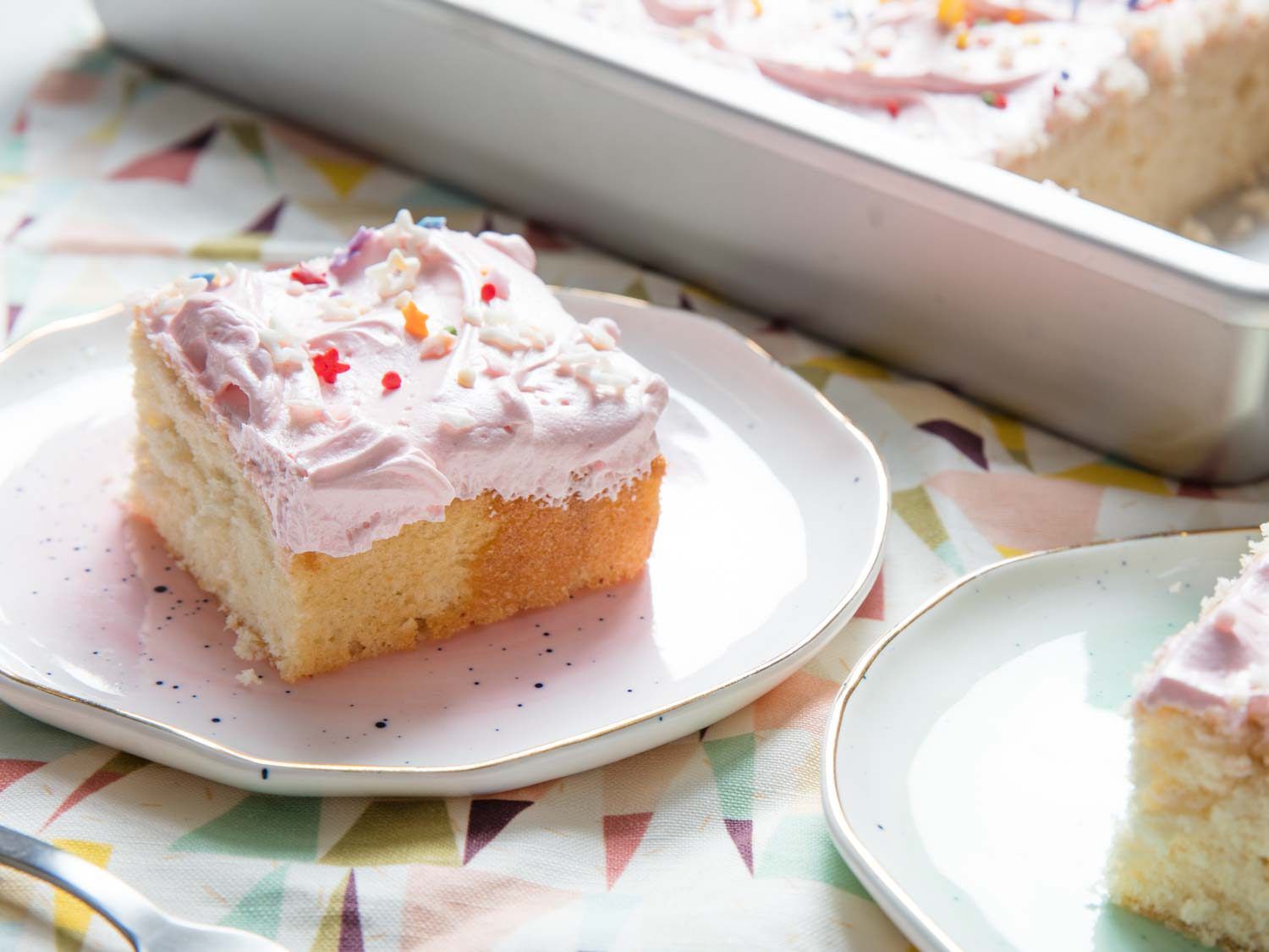 Plated squares of yellow cake iced with pink American buttercream frosting topped with sprinkles