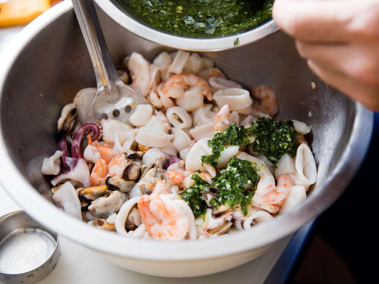Adding dressing of parsley, lemon, and olive oil to prepared seafood in a bowl.