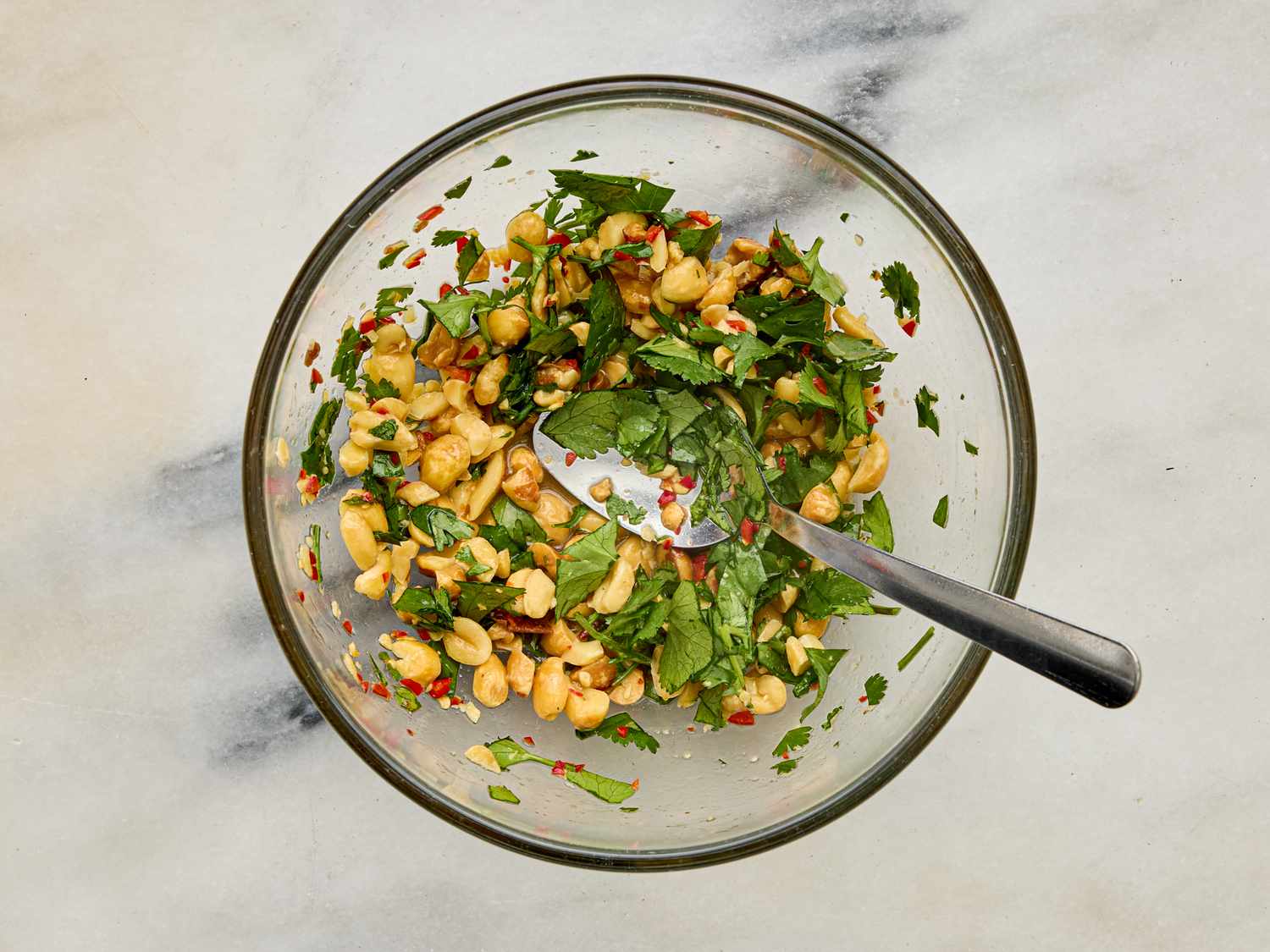 A bowl containing a mixture of herbs peanuts and red chili flakes with a spoon resting in the bowl