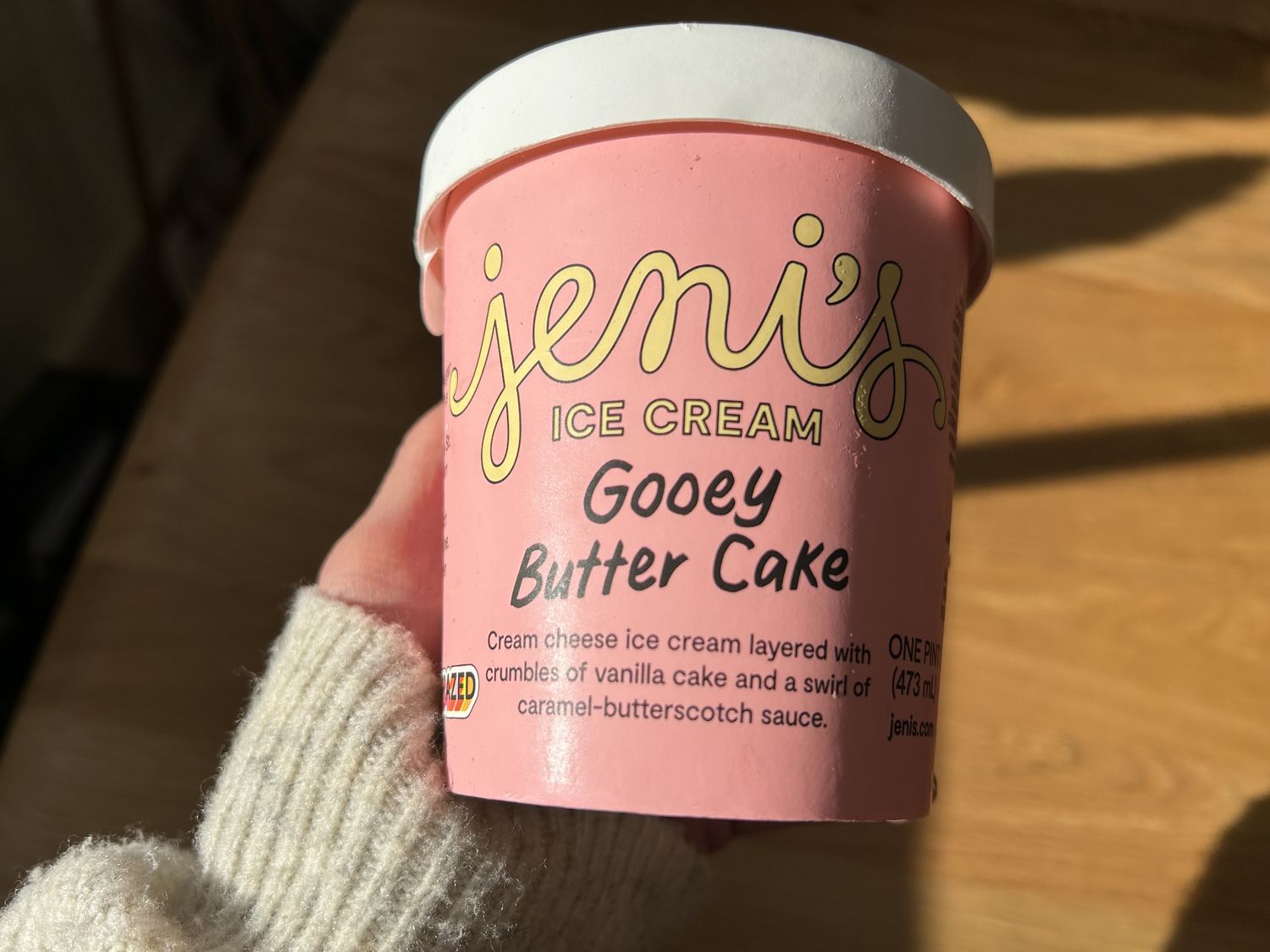 A hand holding a pink tub of Jeni's ice cream