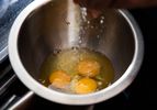 salt being sprinkled into a bowl with raw eggs before whisking