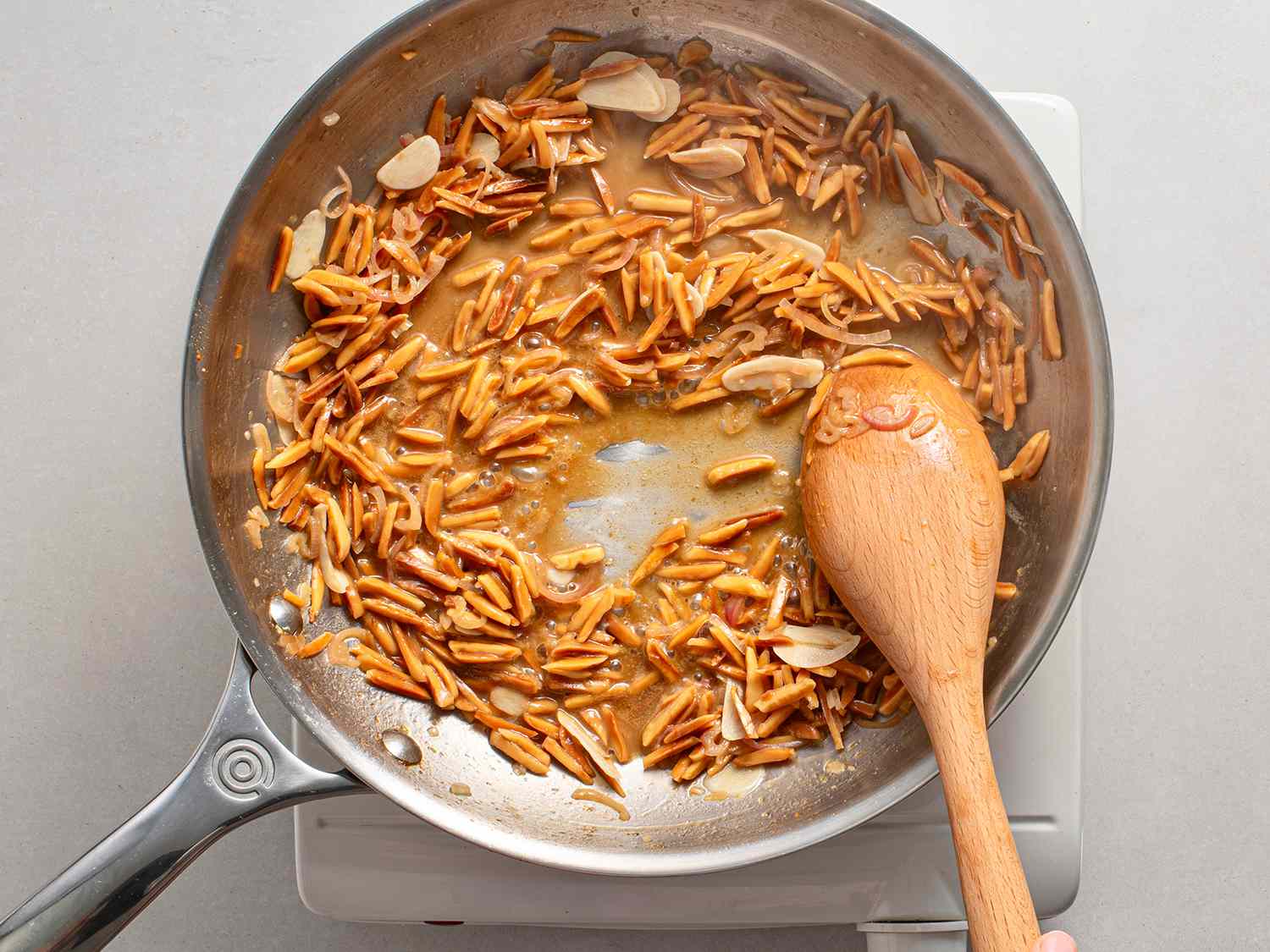 The emulsified pan sauce being stirred in a stainless steel skillet with a wooden spoon.