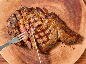 A cooked steak on a wooden board being sliced and held with a fork