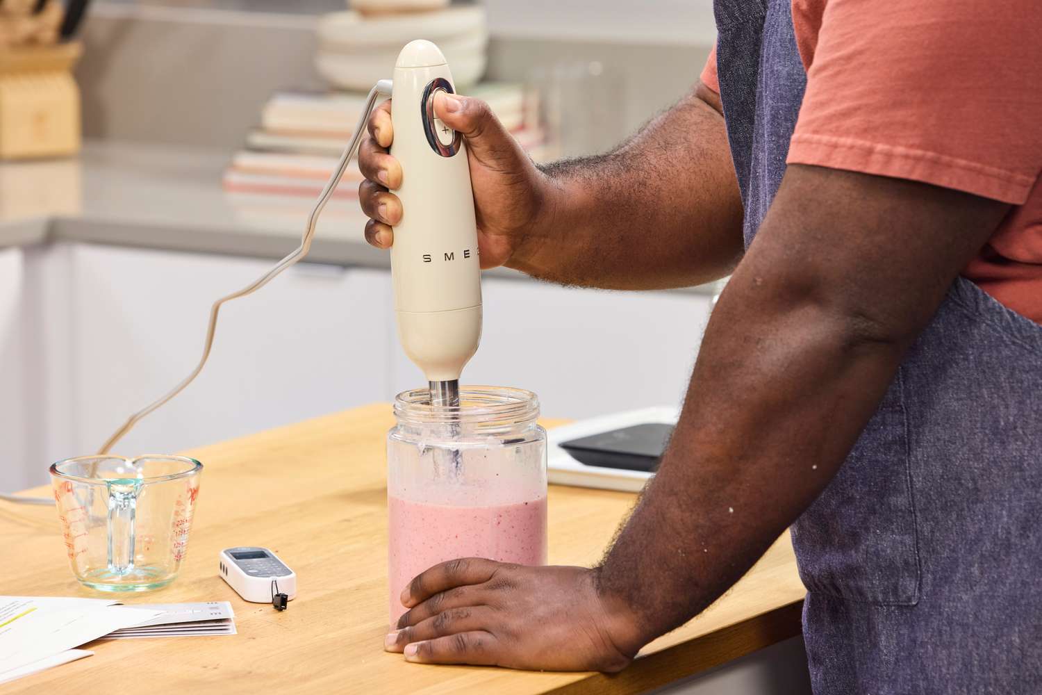 A person makes a smoothie using the Smeg Retro Hand Blender