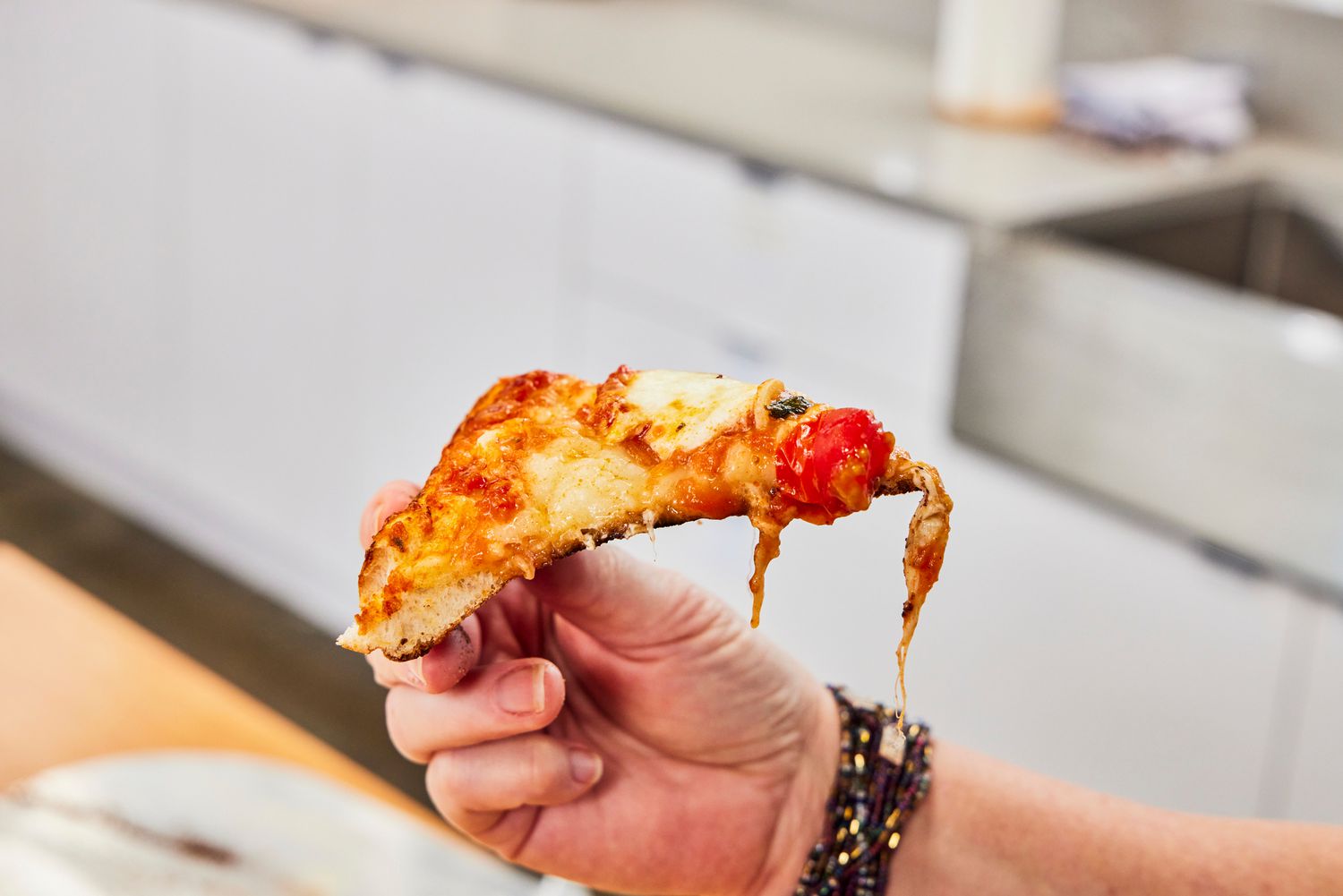 A person lifts up a piece of pizza cooked in the Cuisinart CPZ-120 Stainless Steel Indoor Pizza Oven