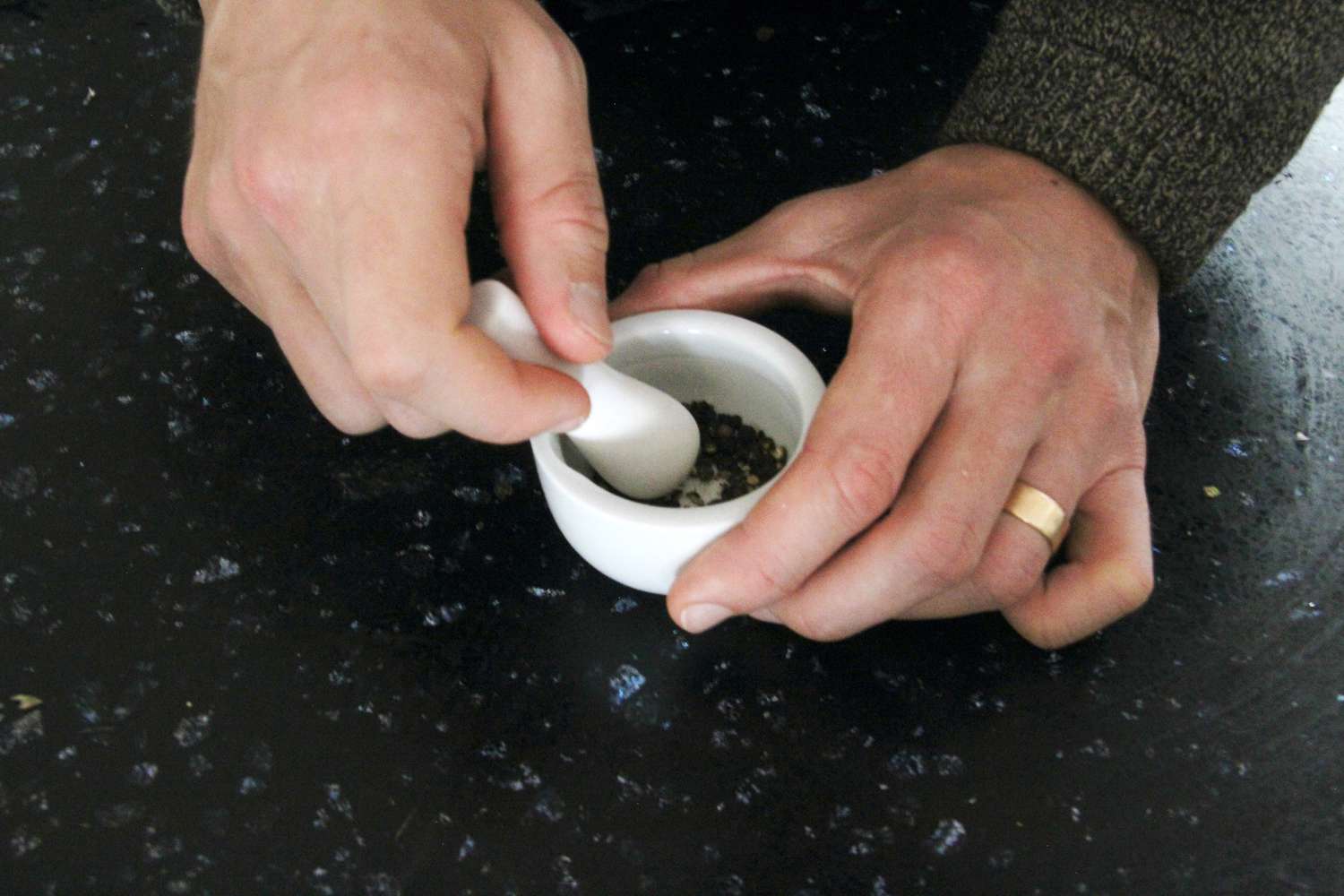 hands using a very tiny pestle to crush black pepper in a very small mortar. 