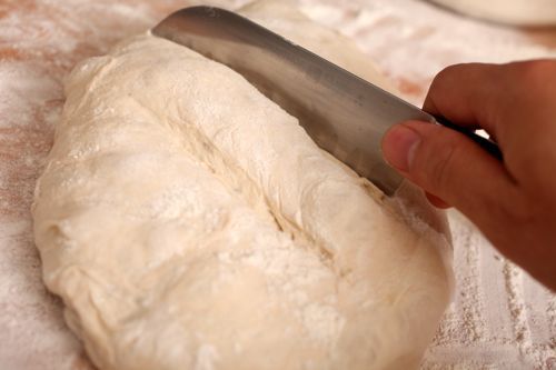 Hand using knife to score top of flour-covered bread dough