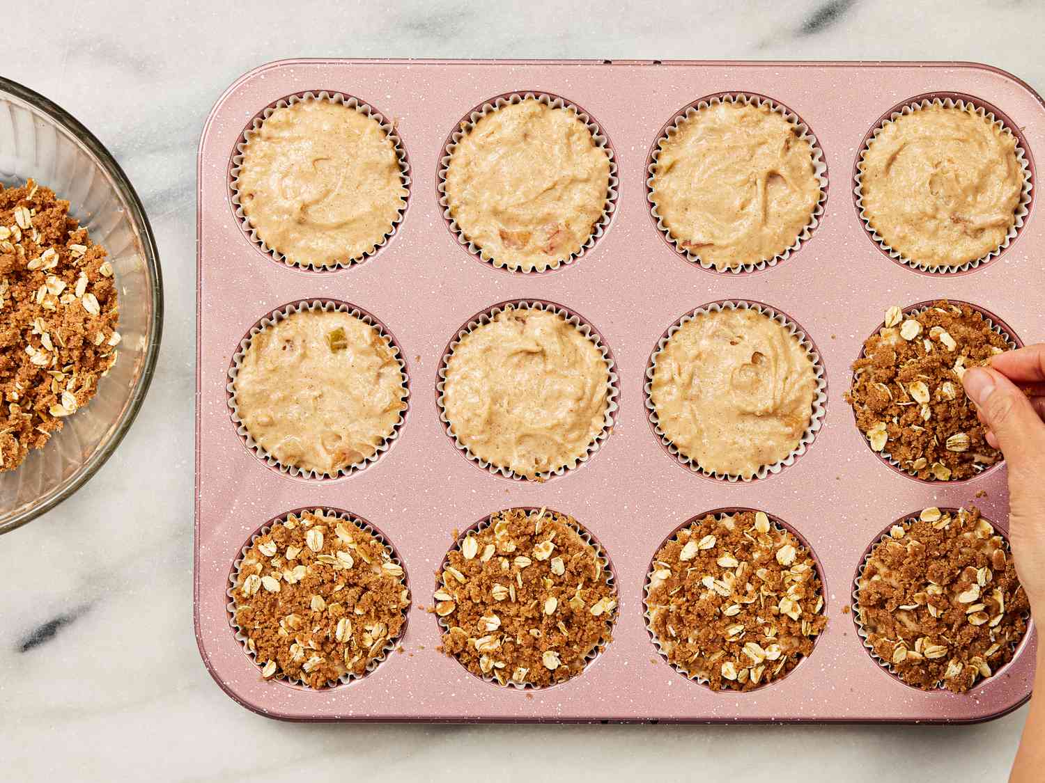 Muffin tin with muffin dough being topped with brown sugar mixture