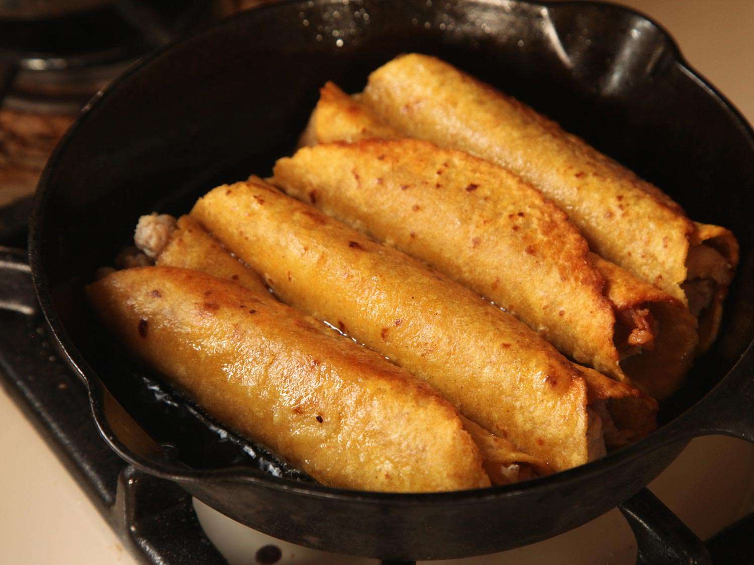 Four enchiladas frying in a cast iron skillet. 