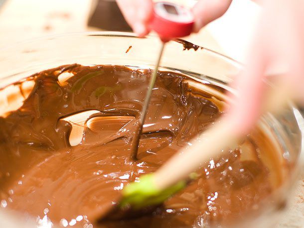 Tempering melted chocolate in a glass bowl with a probe thermometer and a spatula.