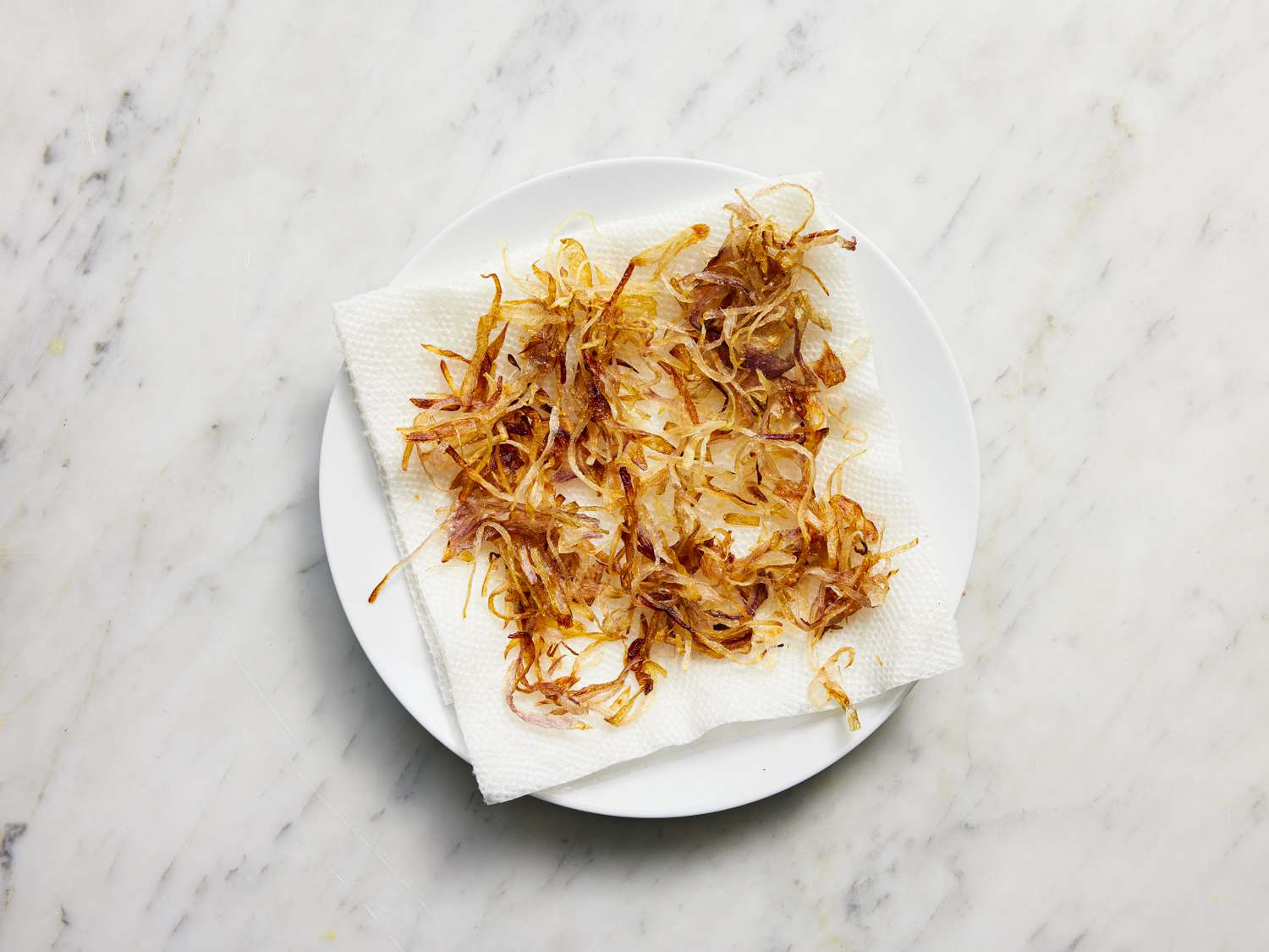 Golden brown fried shallots on a paper towel lined plate