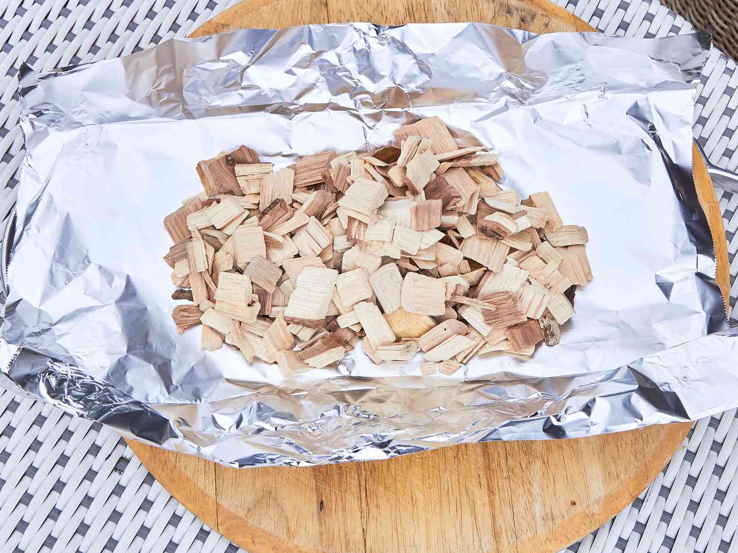 A sheet of aluminum foil containing a pile of wood chips, placed on a wooden surface