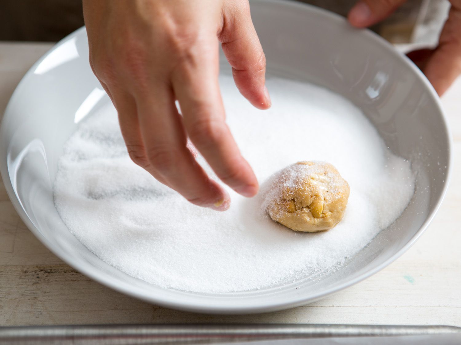 Author rolling a ball of raw cookie dough in a shallow bowl of white sugar. 