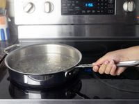 a person holding the handle on a saute pan on the stove top